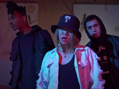 Bailey Sok is wearing a black hat and a white jacket as she is dancing with two male dancers in her background.